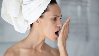 5 Causes of bad breath: image shows woman smelling breath after shower