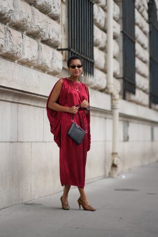 Tamu McPherson wears sunglasses, a red gathered / pleated sleeveless silk lustrous dress, a leather bag, shoes, outside Hermes, during the Womenswear Spring/Summer 2024 as part of Paris Fashion Week on September 30, 2023 in Paris, France.