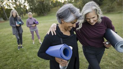 Two older women laugh as they walk arm in arm after a yoga session.