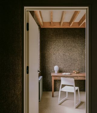 Study with wooden desk, white chair, exposed ceiling beams and dark brown cork walls