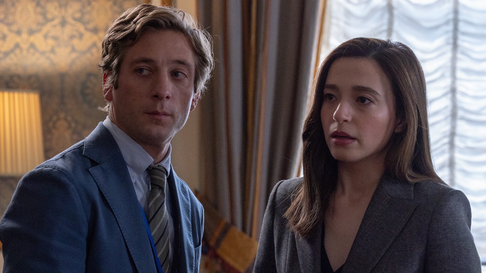 Jeremy Allen White in a blue suit and striped tie, standing next to Mikey Madison in a dark jacket in a room at the Capitol in The Social Reckoning. 