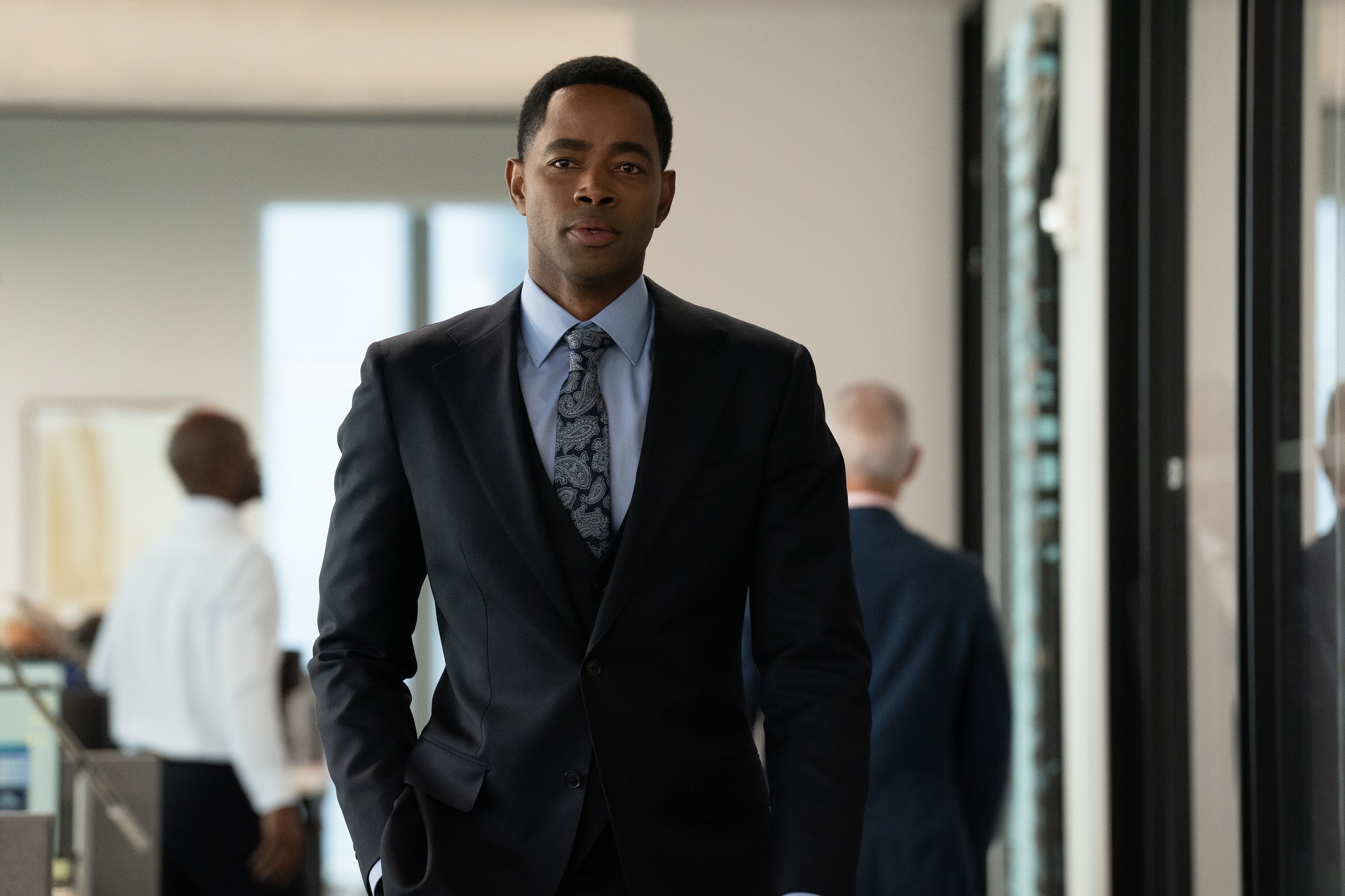 jay ellis as bill gibson wearing a suit walking down a hall at work at a finance job in not suitable for work