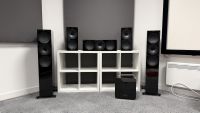 Five black KEF speakers and a black subwoofer arranged on and around a white bookcase