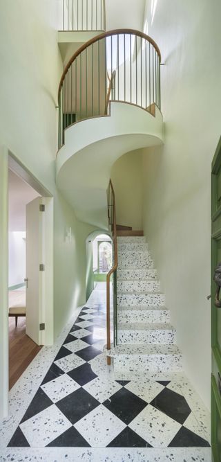 A white marble winding staircase next to a corridor and large open doors.