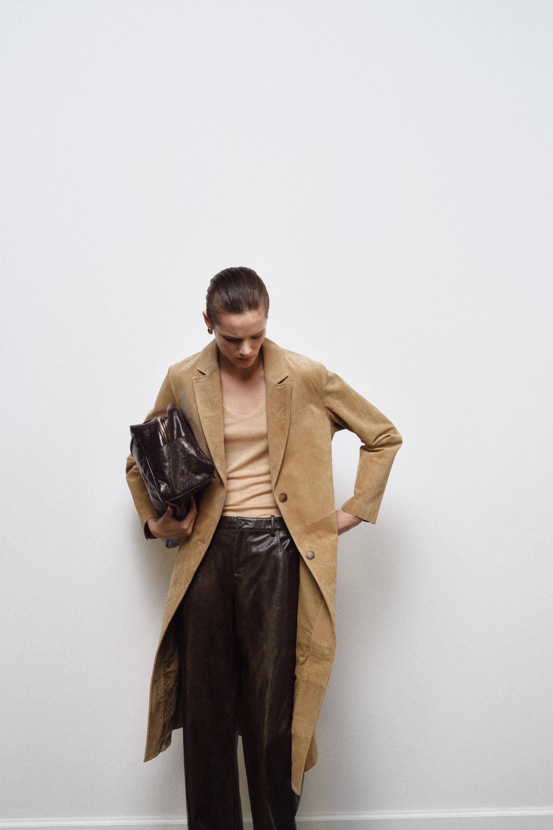 model wears zara outfit that consists of suede coat, tan turtleneck sweater, brown faux leather pants, and black slingbacks while carrying a large tote.