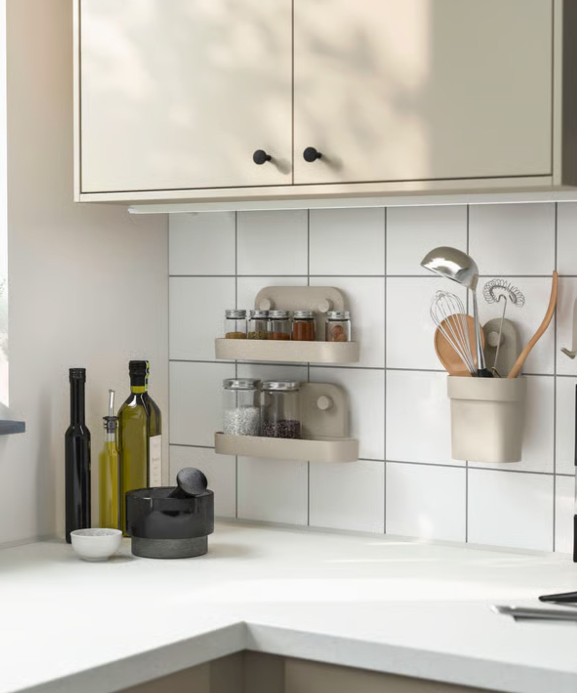 A greige IKEA stick on wall shelf with a shallow rim on a white tile kitchen backsplash beneath matching cabinets. with spice jars inside.