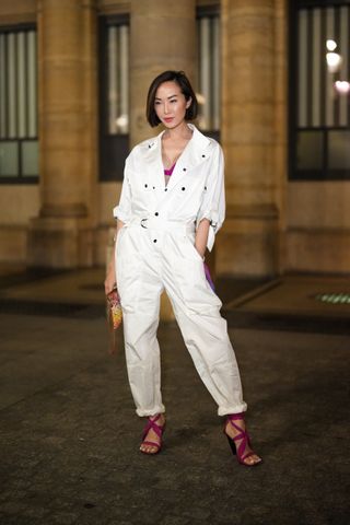 PARIS, FRANCE - MARCH 03: Chriselle Lim wears a pink purple V-neck bra underwear, a white denim buttoned / belted cargo jumpsuit, a braided pink / yellow / orange wickers clutch, purple laces / strappy block heels sandals, outside Isabel Marant, during Paris Fashion Week - Womenswear F/W 2022-2023, on March 03, 2022 in Paris, France. (Photo by Edward Berthelot/Getty Images)