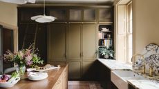 A kitchen with olive green cabinets, marble countertops, and a wooden island