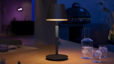 PHILIPS Hue Go Smart Portable Table Lamp style on a wooden patio table alongside a fluted carafe set