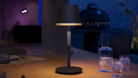 PHILIPS Hue Go Smart Portable Table Lamp style on a wooden patio table alongside a fluted carafe set
