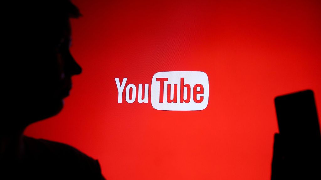 A person holds a phone in front of the YouTube logo.