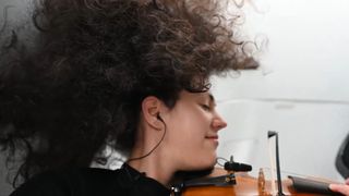 a woman plays violin while floating in zero gravity inside a white spacecraft cabin