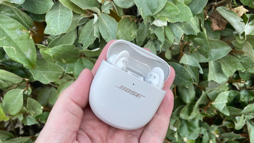 Bose QuietComfort Ultra Earbuds in their case in front of a green hedge