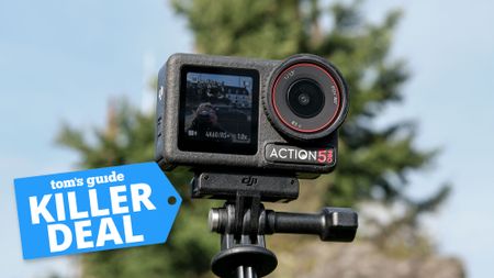 The DJI Osmo Action 5 Pro on a selfie stick with a green tree and blue sky out of focus in the background