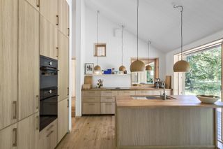 Solid wood kitchen flooring in a natural scheme with wooden cabinets, white walls and pendant lighting.