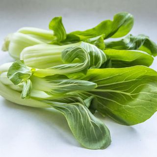 Three heads of green pak choi laying on their side on a grey worktop 