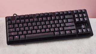 Top-down view of Razer Huntsman V3 Tenkeyless 8KHz on desk with RGB backlighting on, with pink wall in background