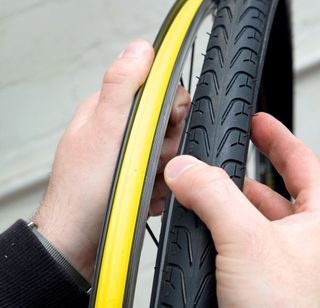 fix an inner tube mend a puncture image shows a pair of hands with the tyre in the right and wheel in the left