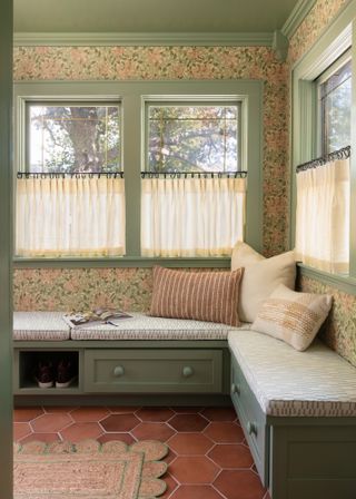 Bench seating underneath a window painted green with terracotta floor