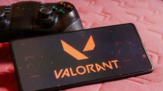 The Valorant logo is displayed on a smartphone screen, next to an Xbox controller