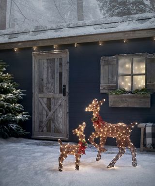 Two deer lights outside snowy house