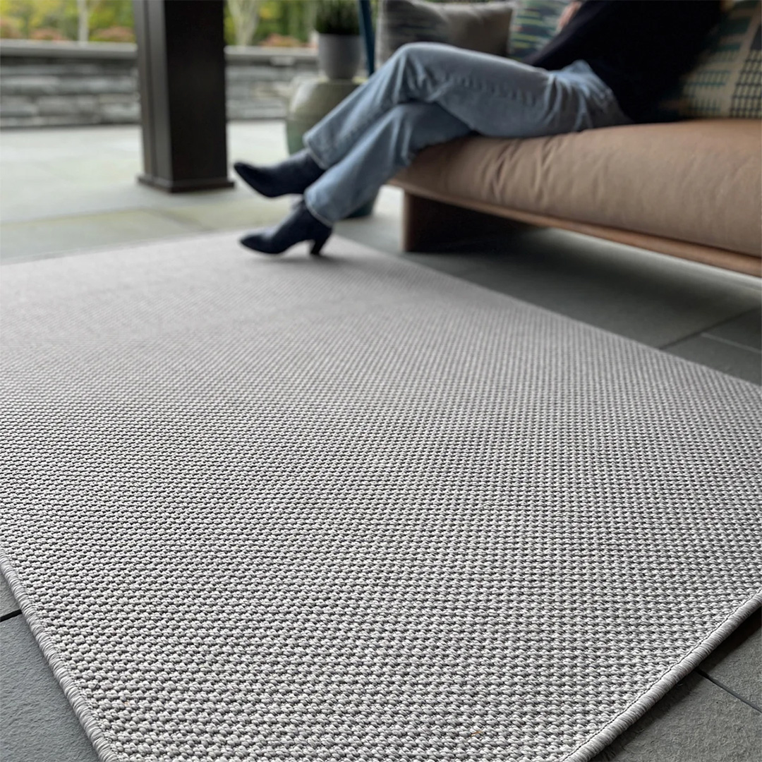 Woven mat on a floor showing a couch nearby with person sitting on it