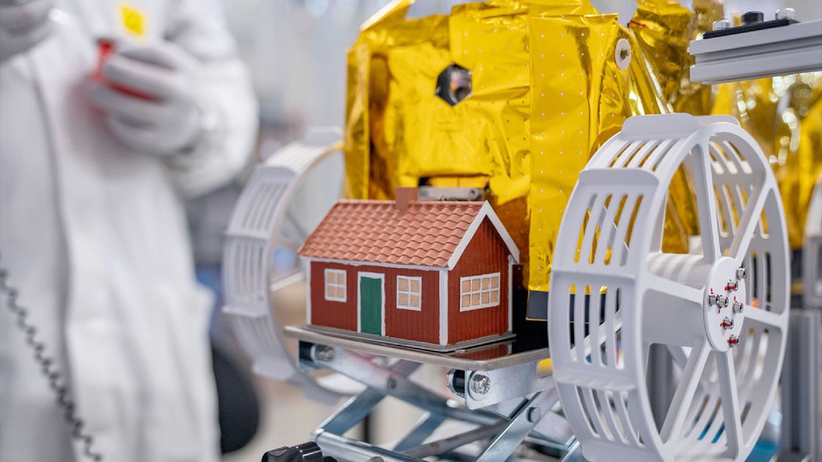 a small model of a red and white house is mounted to a gold foil-covered lunar rover with white wheels