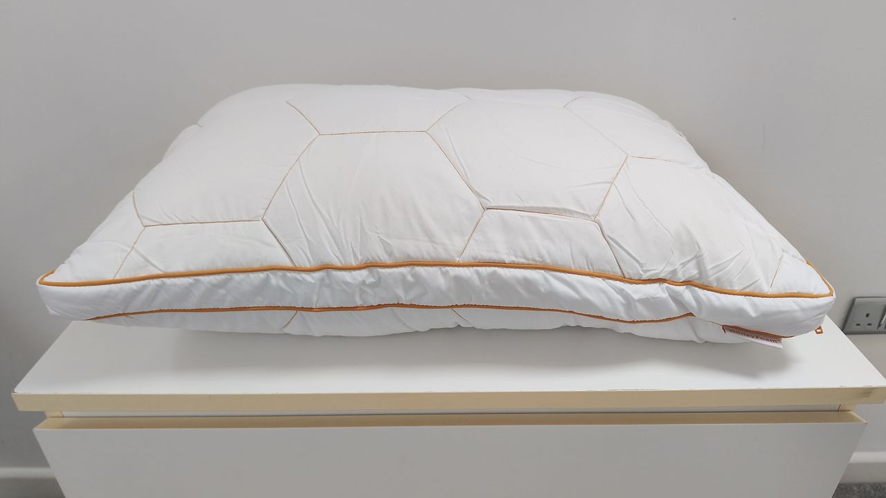 A white bed pillow with a geometric hexagonal quilted pattern and orange piping sitting on a white surface.