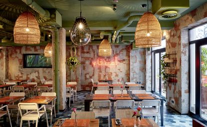 Restaurant with tables, chairs, patterned coloured walls and large pendant lights at Bar Skuka, Frankfurt, Germany.