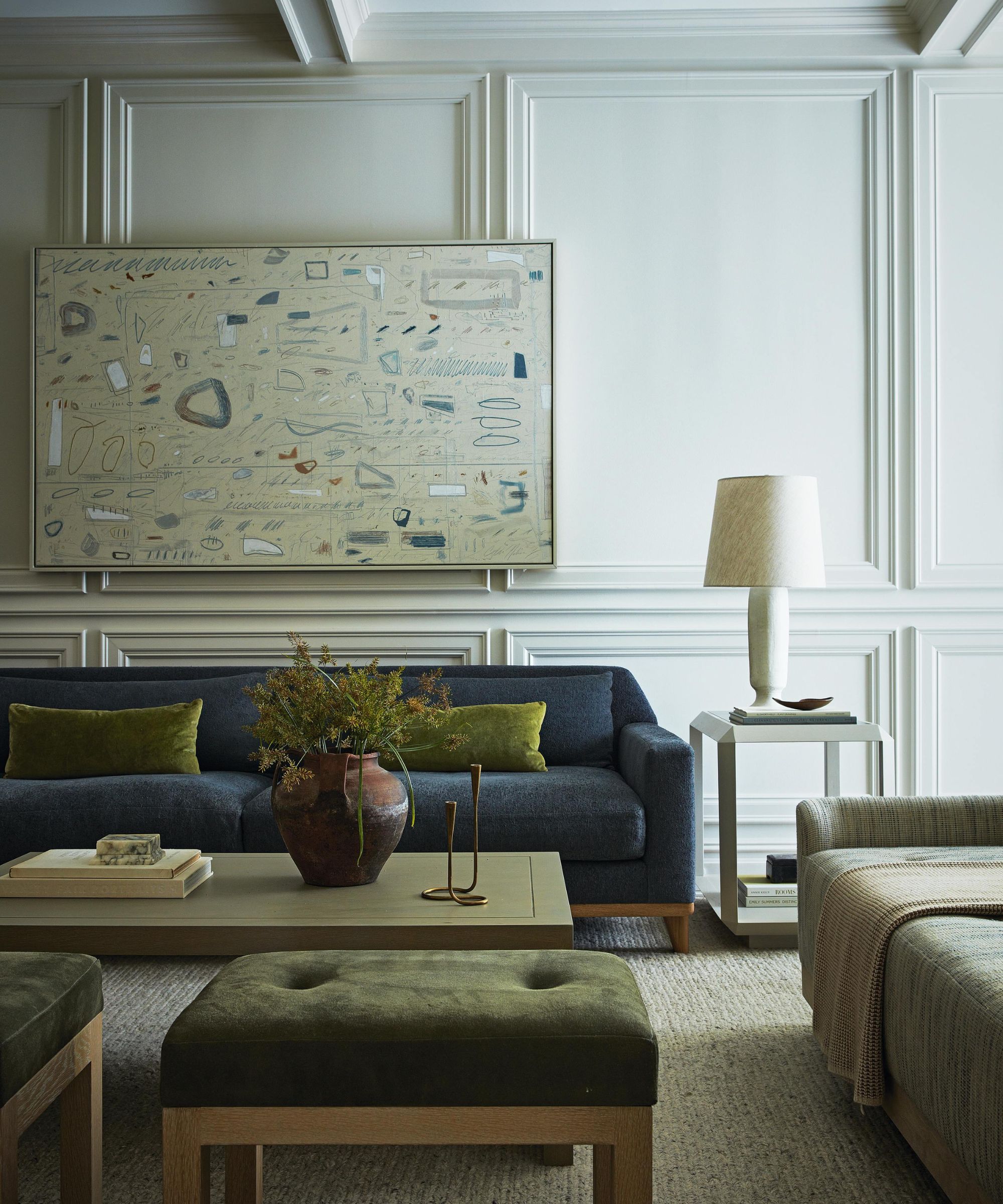 a light sitting room with wall molding, a navy couch, small green ottomans, and abstract artwork