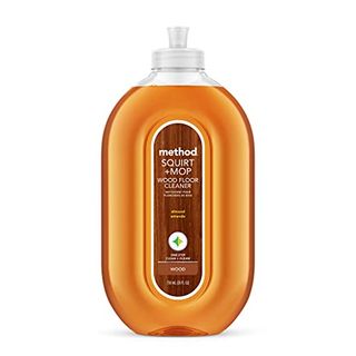 A rounded clear plastic bottle with orange liquid inside. A wood patterned label with method branding in the middle.