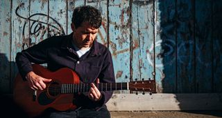 Neil Thomas of Pavey Ark plays his Martin OM-1 in front of a blue door with distressed paint.