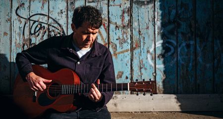 Neil Thomas of Pavey Ark plays his Martin OM-1 in front of a blue door with distressed paint.