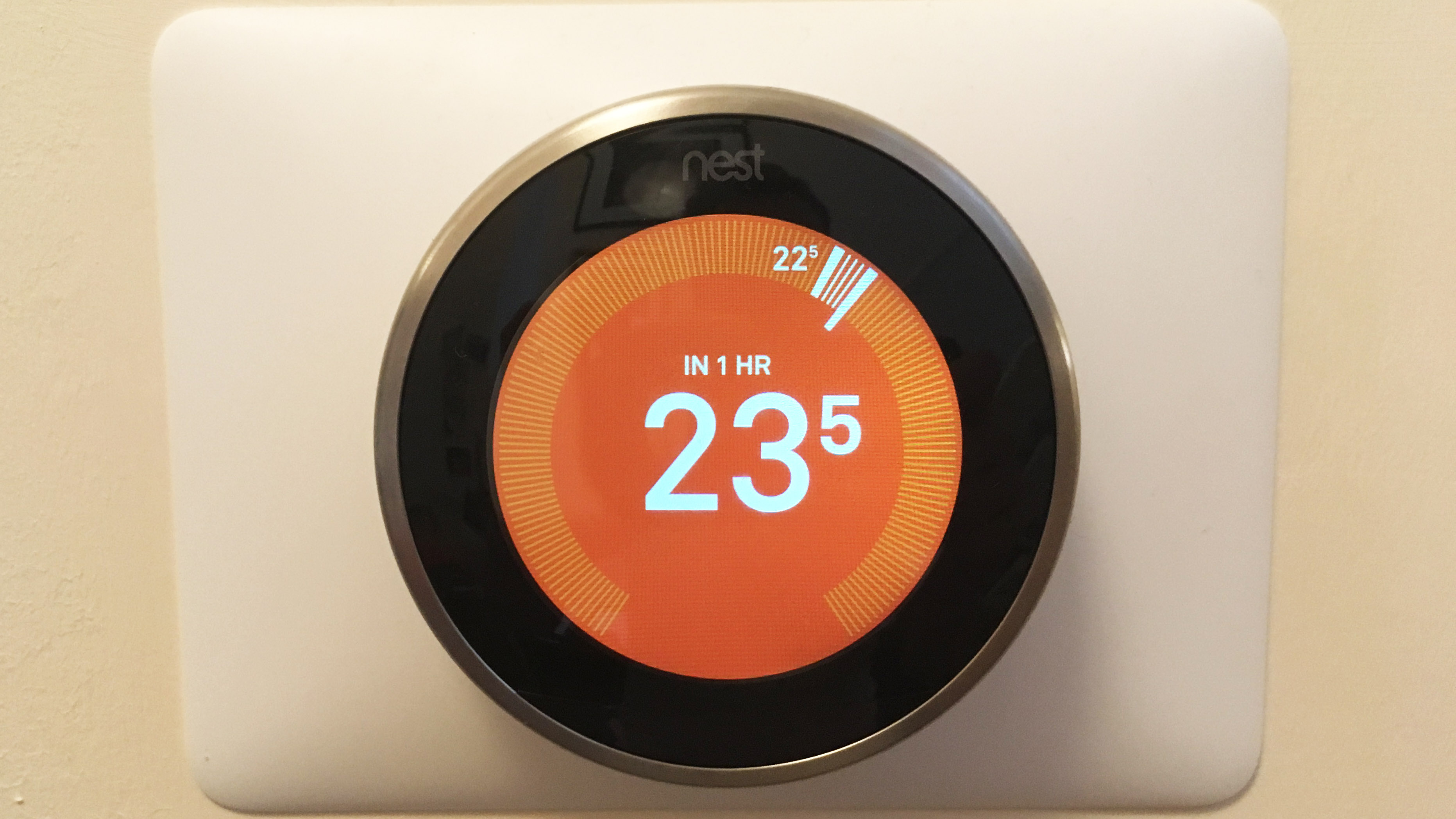 En Nest Learning Thermostat sitter på en vägg och visar temperaturen på en orange skärm.