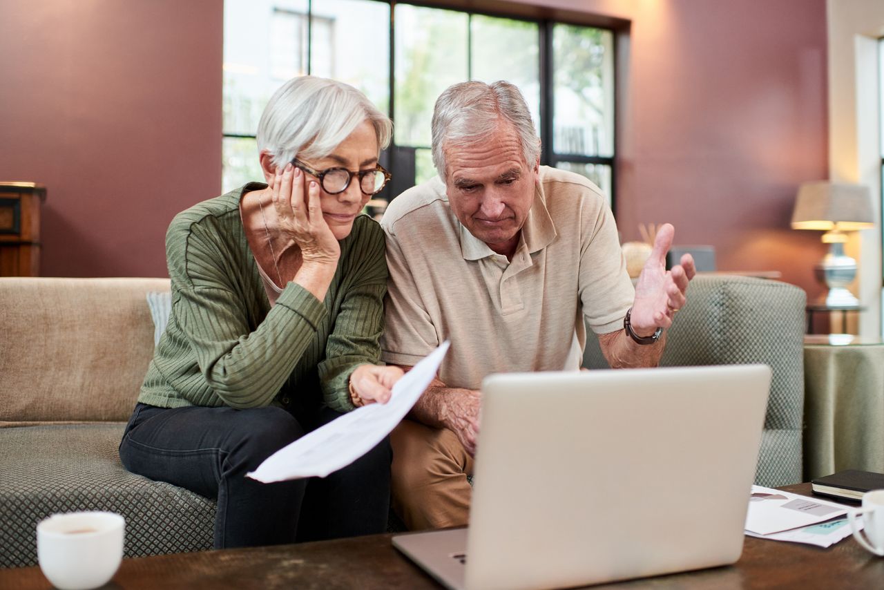 Shot of a senior couple using a laptop while going through paperwork at home.