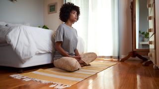 A woman meditates by her bed