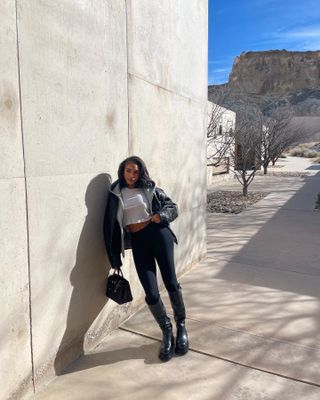 Model Lori Harvey wears black leggings, zip-up sweater, white t-shirt, and black bag.