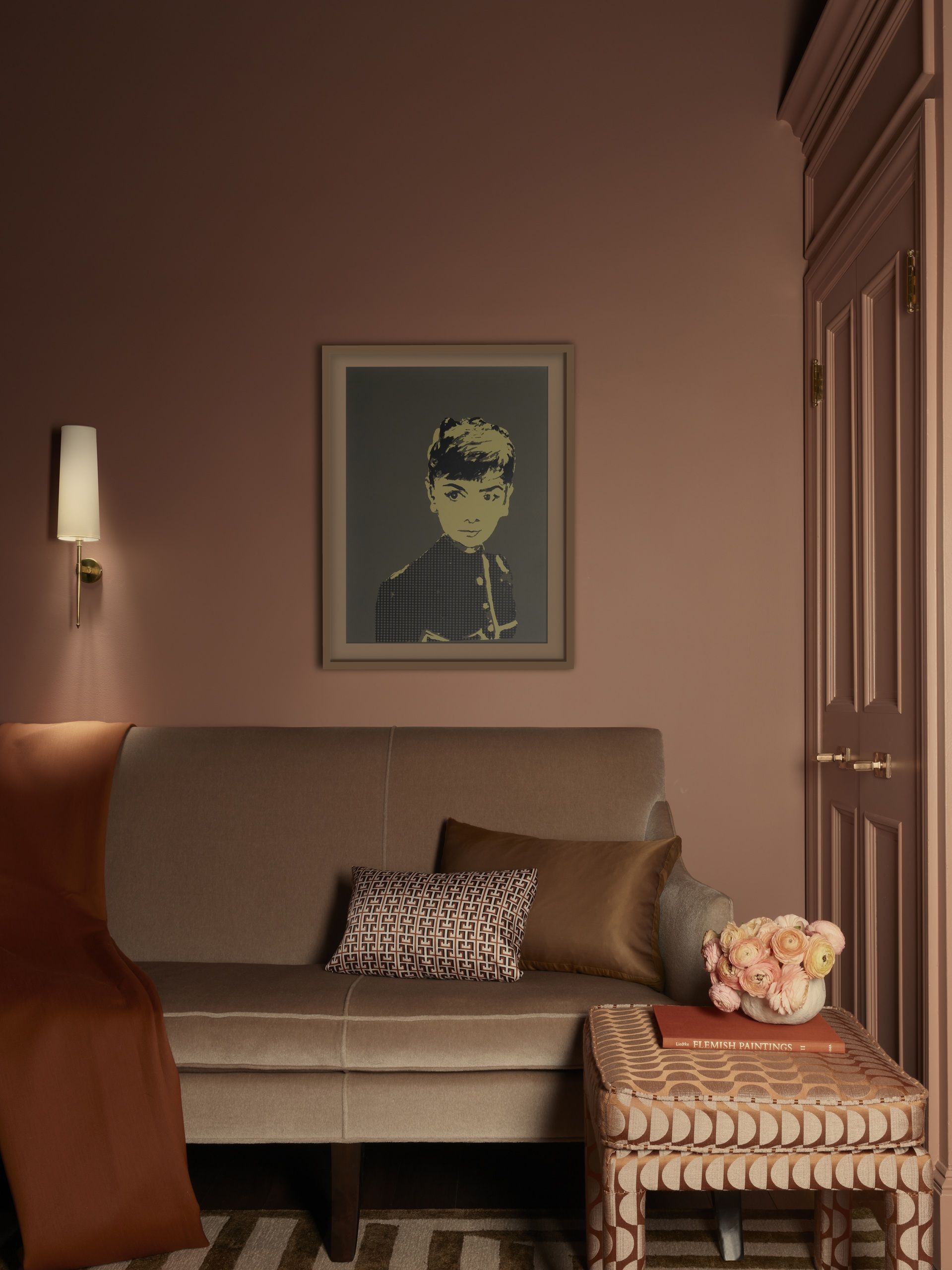 a tonal pink room with a velvet sofa and audrey hepburn artwork