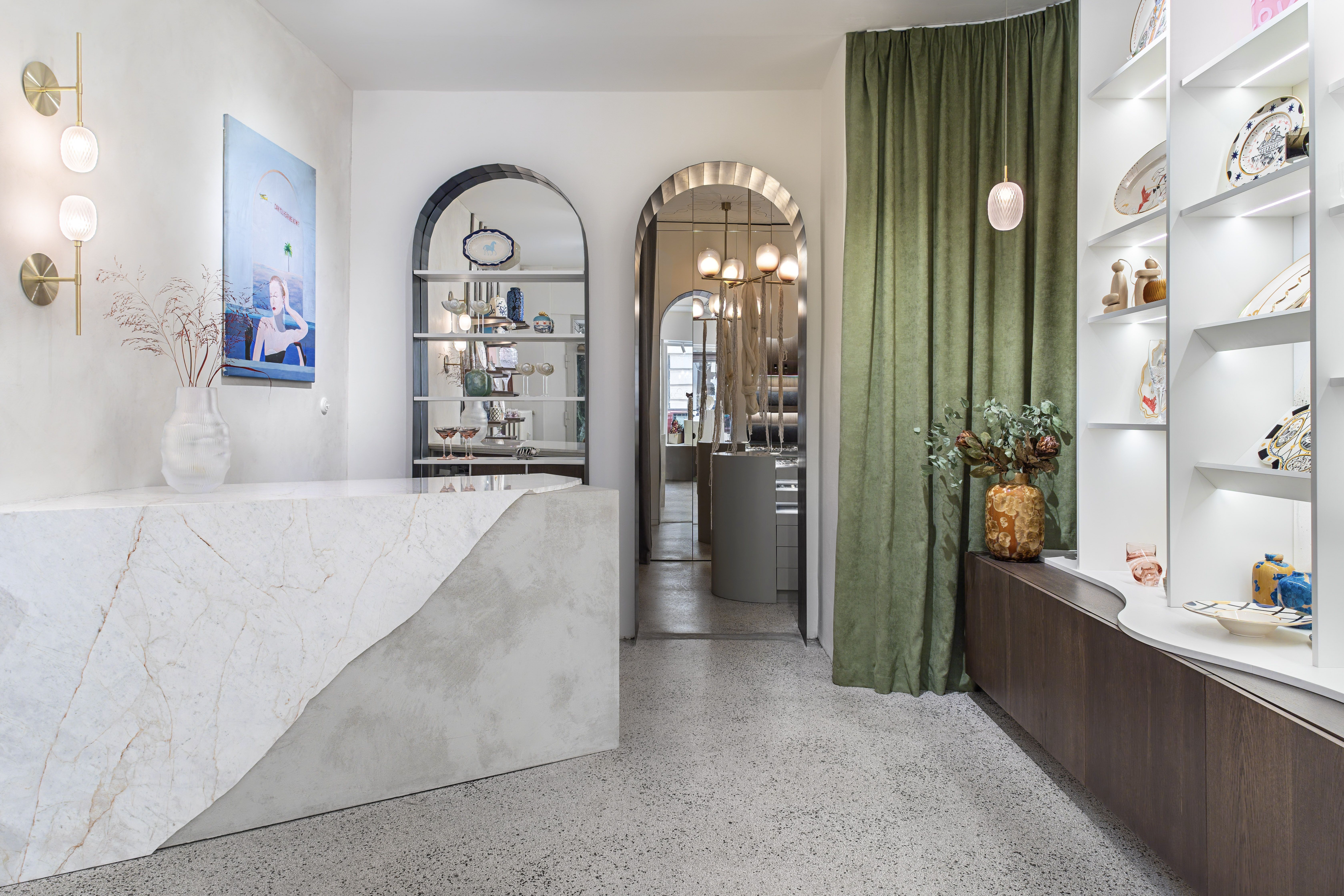 The interior of a design shop, with green curtains, a sculptural countertop, and colorful collectibles.
