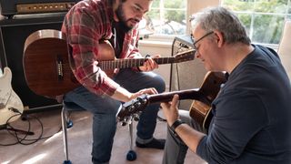Younger man teaching older man how to play guitar 