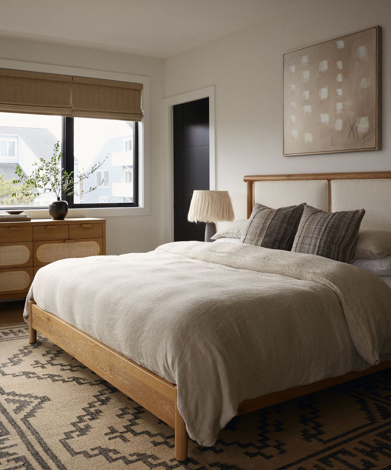 A coastal modern bedroom with a wooden bedframe, a patterned rug, and a console table