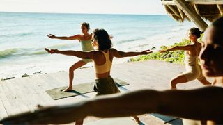 Woman stretching with others in yoga class retreat by the sea, in the sunshine