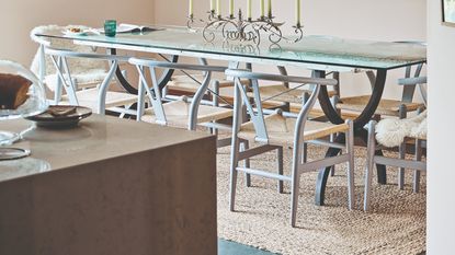 A dining room with a rectangular glass table and a jute rug underneath