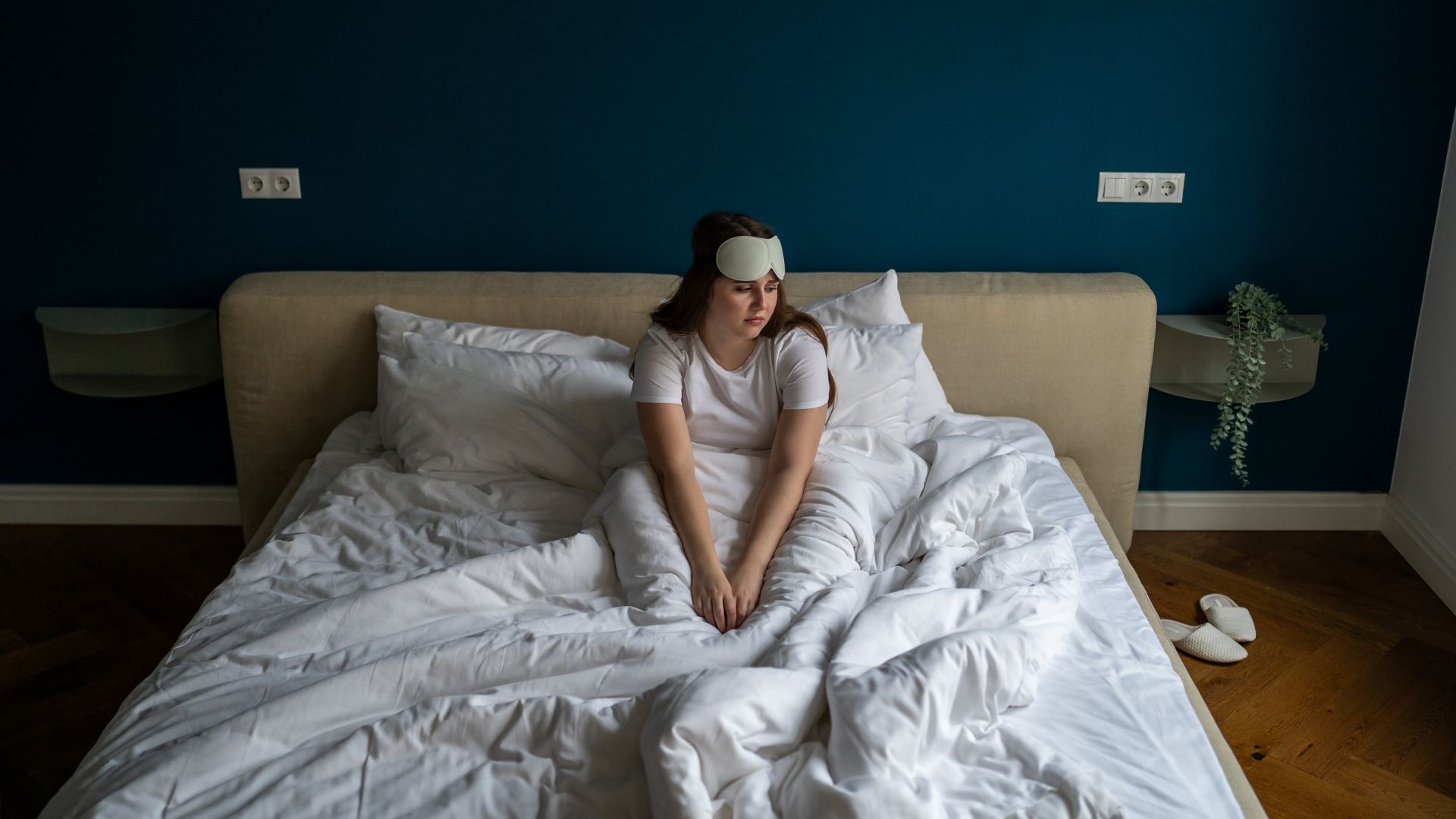 A woman sits up in bed in the middle of the night looking unhappy.