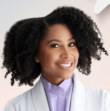 a black woman with a dark afro wearing a white lab coat and lavender shirt smiling at the camera
