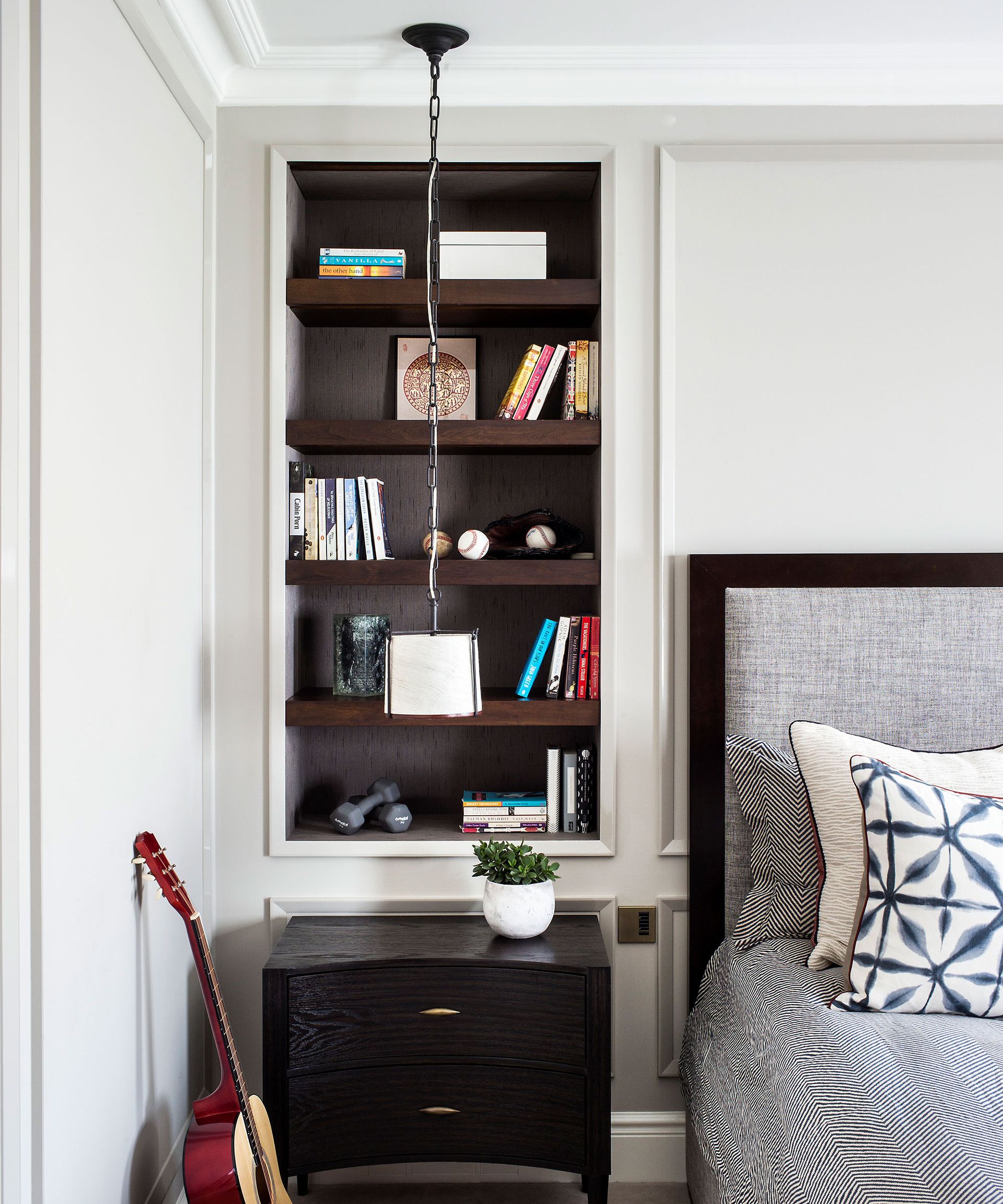 An example of bedroom lighting ideas showing a monochrome bedroom with built in shelving next to the bed