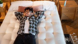 Man lying on his bed on a new mattress with his hands behind his head smiling