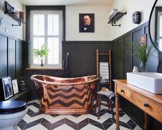 A bathroom with copper bath, chevron flooring and wall art