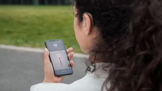 A young woman wears the Oticon Xceed SP and uses the app on her iPhone to adjust the aid's volume