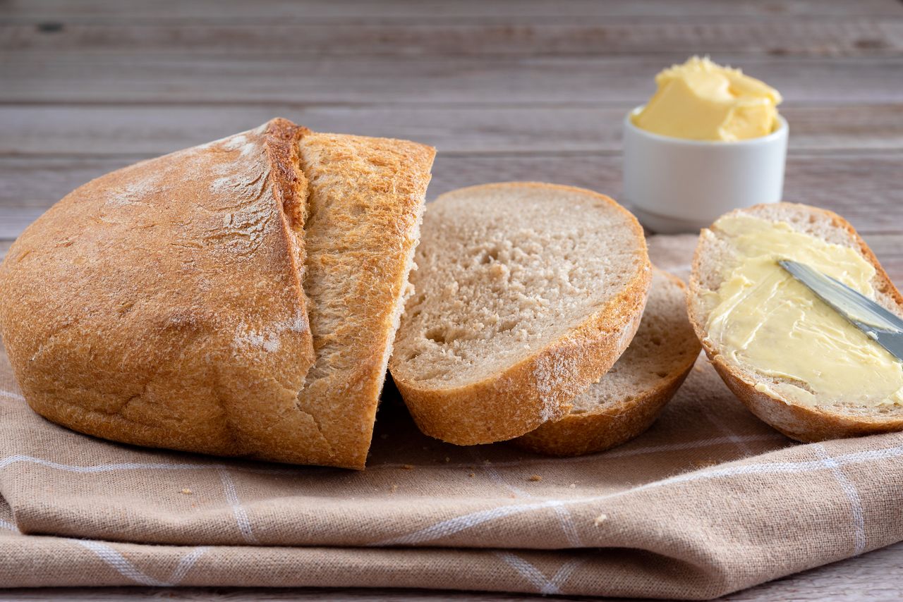 Cob loaf sliced on a tea towel with a piece of bread smothered with butter